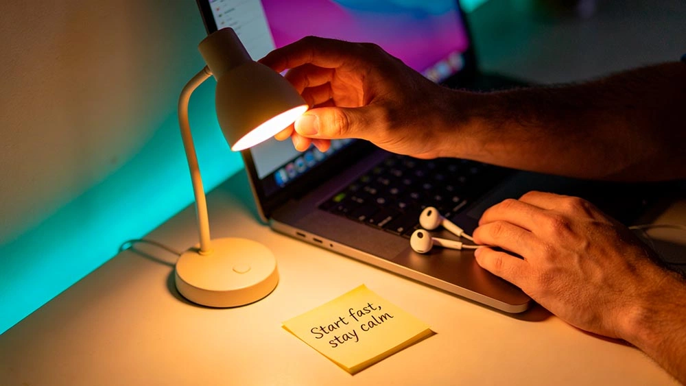 talk to women online quickly: 60-second checklist talk to women online quickly: simple checklist vibe, man using earbuds and adjusting a small desk lamp for better video call lighting